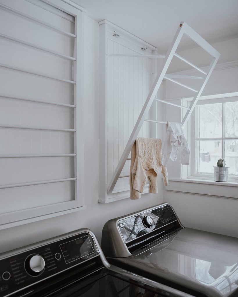 The Wild Decoelis | Laundry room makeover with grey cabinets, hexagon white tile and butcher block countertops, wall mounted drying racks