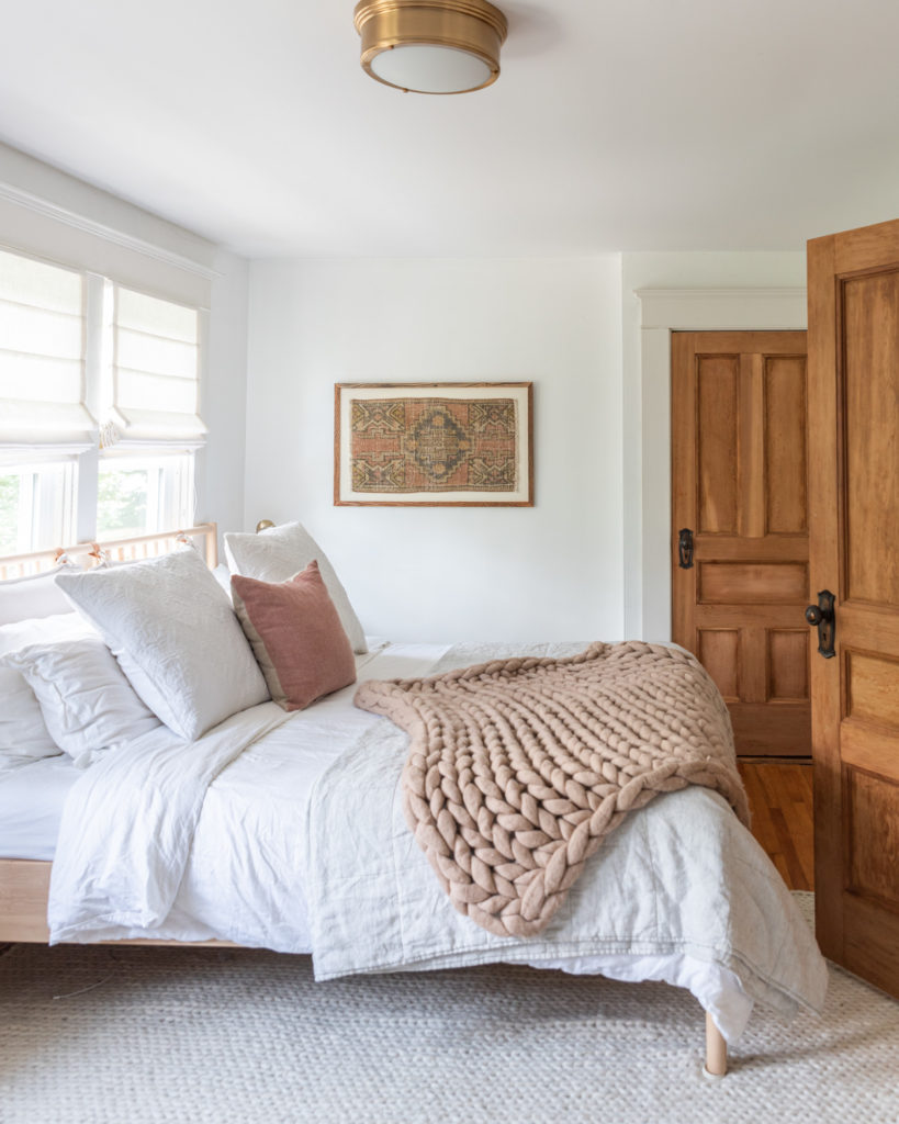 De Wilde Decoelis / Hoe maak je een DIY ingelijst Vintage tapijt voor minder dan $ 100 | turks tapijt in diy houten frame, Master bedroom met wit dekbedovertrek en linnen bedcover met blush grote gebreide deken, Ikea Bjorksnas bedframe baby van venster met bijpassende tafel. 