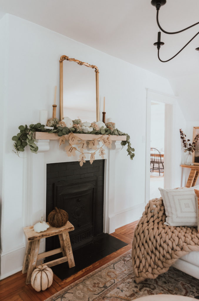 The Wild Decoelis | Fall Home Tour | mantle decorated with faux eucalyptus bows, vintage candlesticks, gold leaf mirror, Thanksgiving banner, dried hydrangeas, and white pumpkins