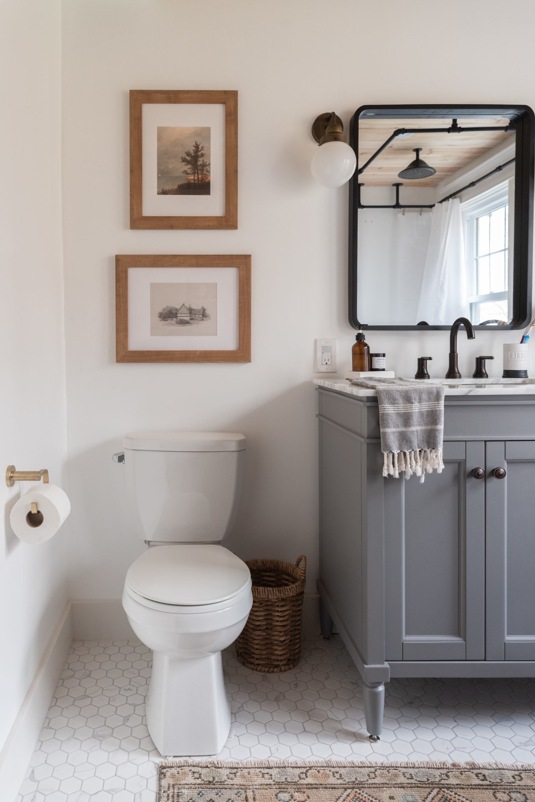 The Wild Decoelis | Our Bathroom Reno | white bathroom with gray vanity, marble hexagon floor tiles and marble countertop, black clawfoot tub, cedar plank ceiling, and an antique refinished black china cabinet used for linens