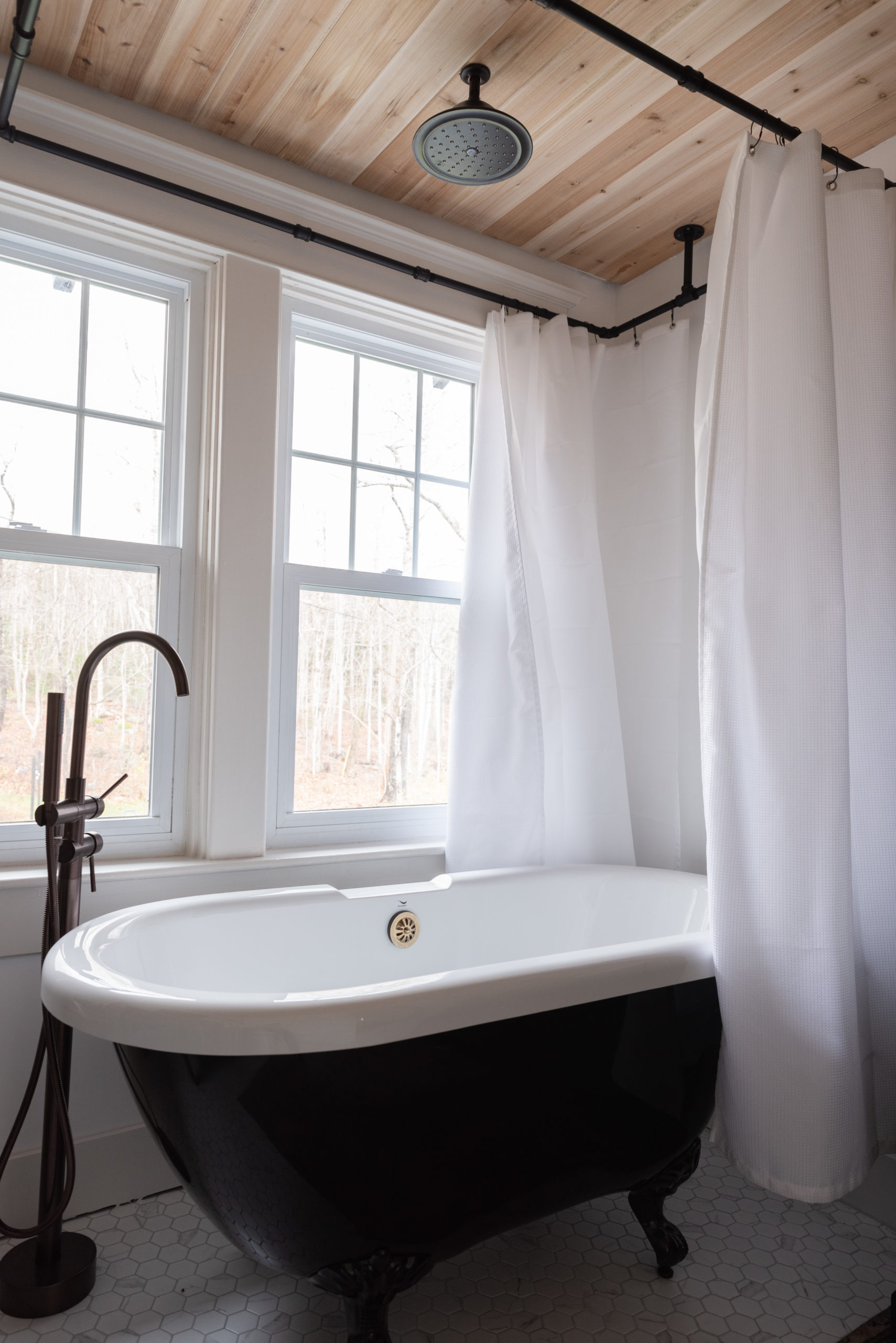 The Wild Decoelis | Our Bathroom Reno | white bathroom with gray vanity, marble hexagon floor tiles and marble countertop, black clawfoot tub, cedar plank ceiling, and an antique refinished black china cabinet used for linens