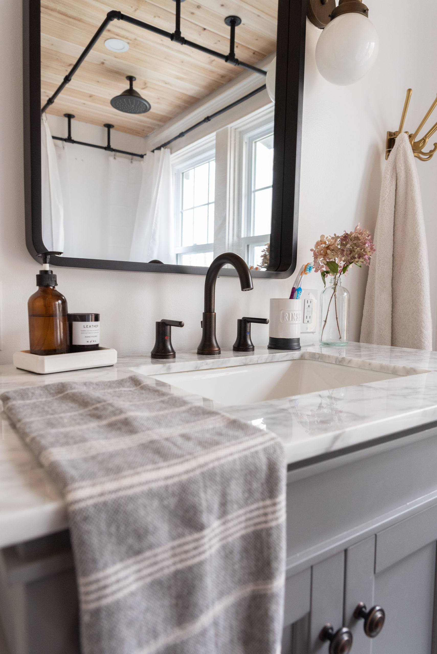 The Wild Decoelis | Our Bathroom Reno | white bathroom with gray vanity, marble hexagon floor tiles and marble countertop, black clawfoot tub, cedar plank ceiling, and an antique refinished black china cabinet used for linens