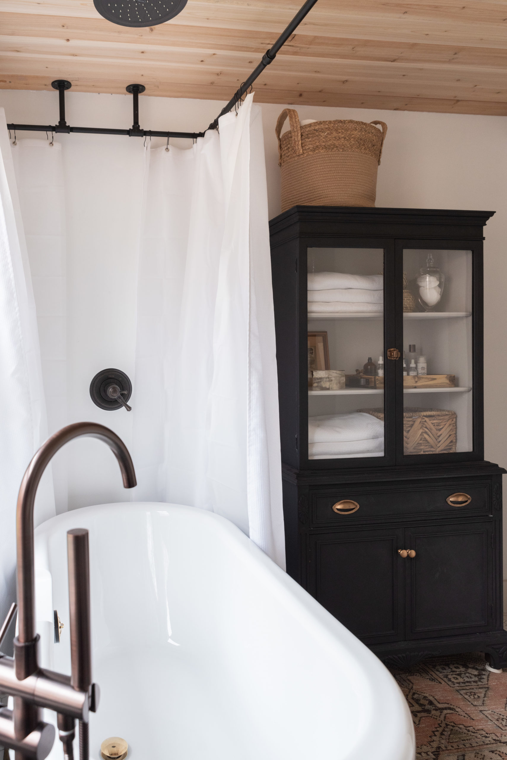 The Wild Decoelis | Our Bathroom Reno | white bathroom with gray vanity, marble hexagon floor tiles and marble countertop, black clawfoot tub, cedar plank ceiling, and an antique refinished black china cabinet used for linens