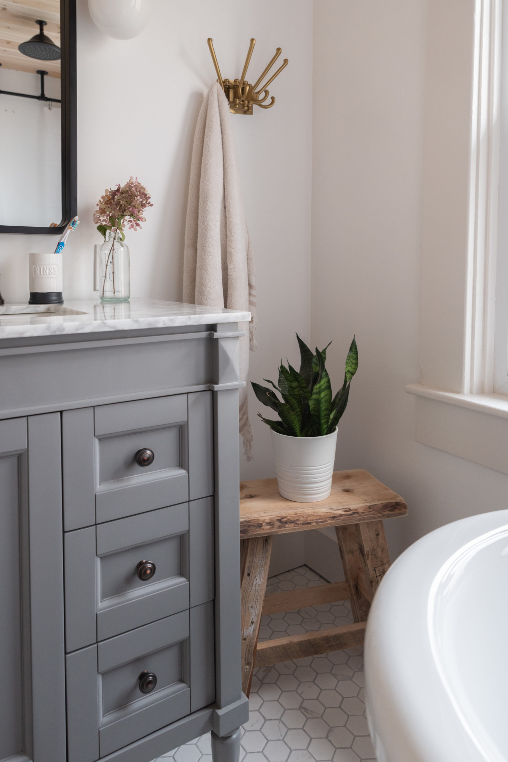 The Wild Decoelis | Our Bathroom Reno | white bathroom with gray vanity, marble hexagon floor tiles and marble countertop, black clawfoot tub, cedar plank ceiling, and an antique refinished black china cabinet used for linens