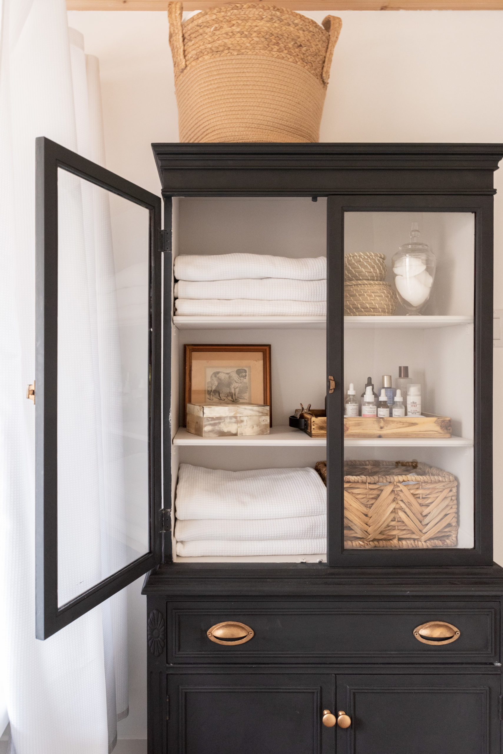 The Wild Decoelis | Our Bathroom Reno | white bathroom with gray vanity, marble hexagon floor tiles and marble countertop, black clawfoot tub, cedar plank ceiling, and an antique refinished black china cabinet used for linens