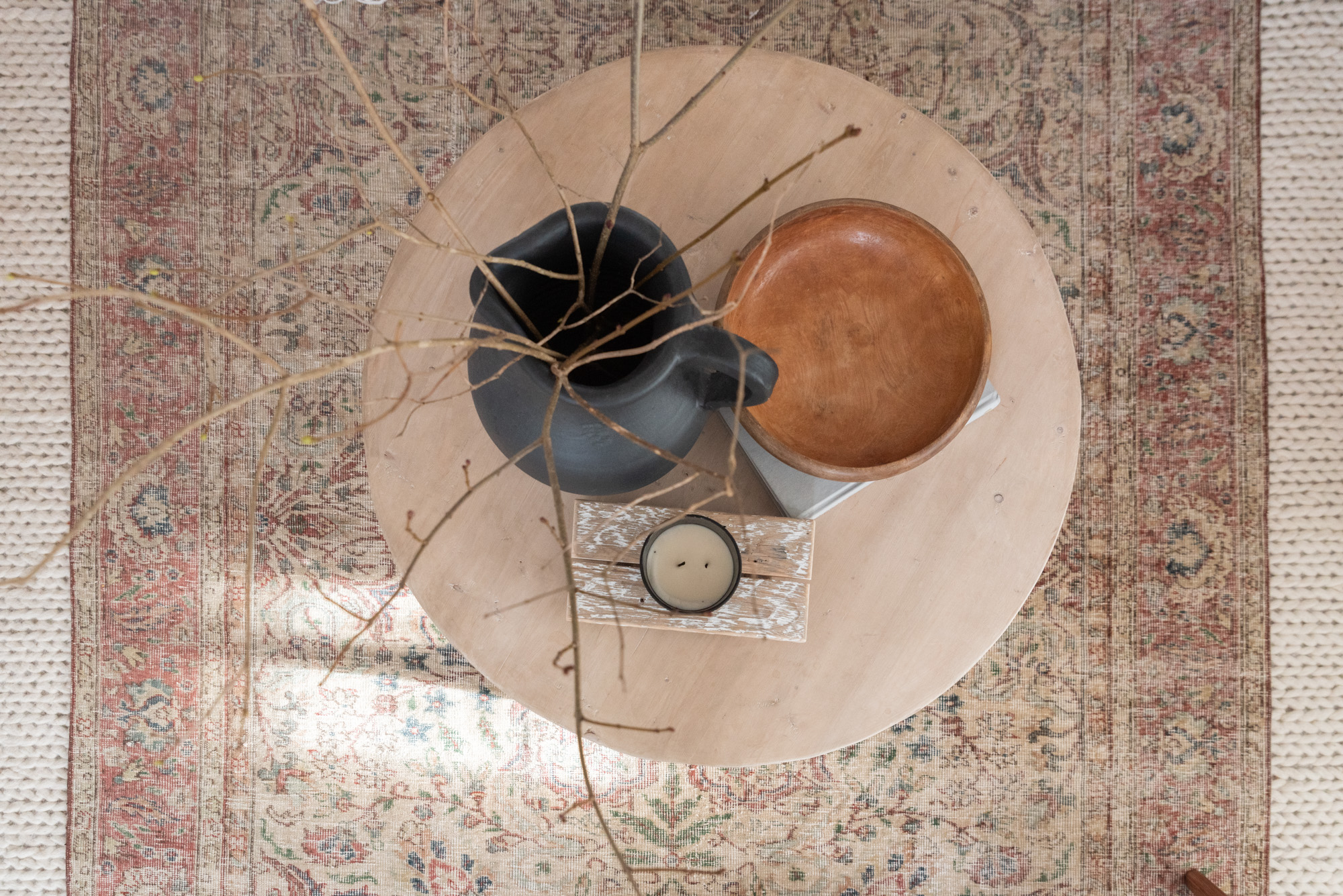 The Wild Decoelis | how to decorate for winter | cream couch with vintage wool rug layers over cream braided rug. wool pillows, sticks in a vase, fireplace with candles. layering a coffee table