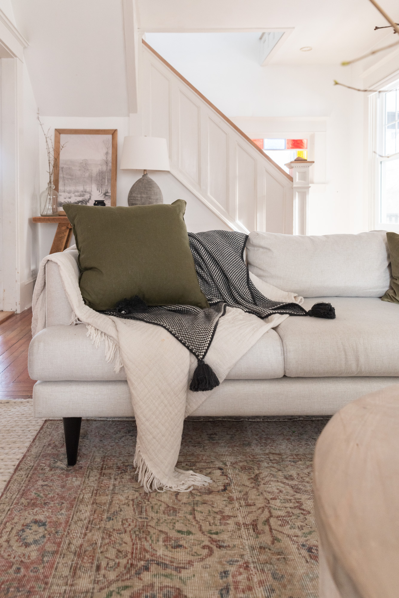 The Wild Decoelis | how to decorate for winter | cream couch with vintage wool rug layers over cream braided rug. wool pillows, sticks in a vase, fireplace with candles. layering throw pillows and blankets