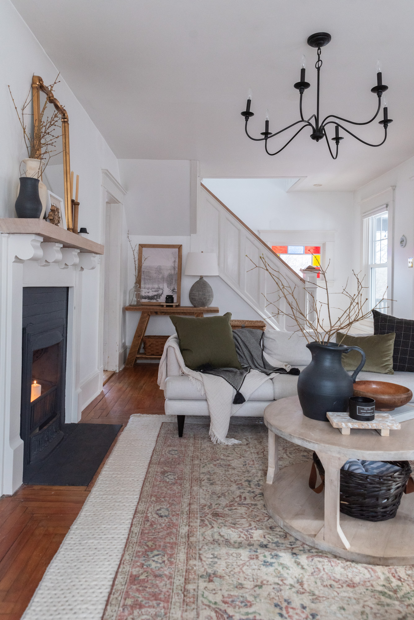 The Wild Decoelis | how to decorate for winter | cream couch with vintage wool rug layers over cream braided rug. wool pillows, sticks in a vase, fireplace with candles