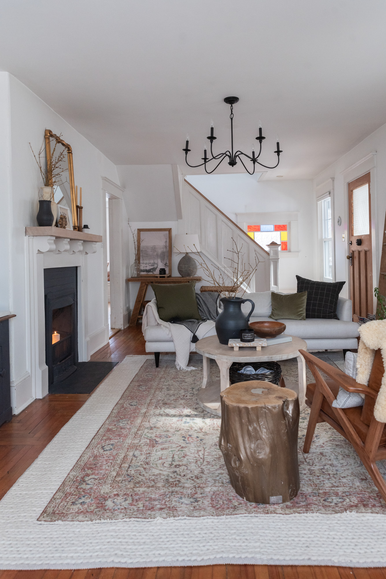 The Wild Decoelis | how to decorate for winter | cream couch with vintage wool rug layers over cream braided rug. wool pillows, sticks in a vase, fireplace with candles