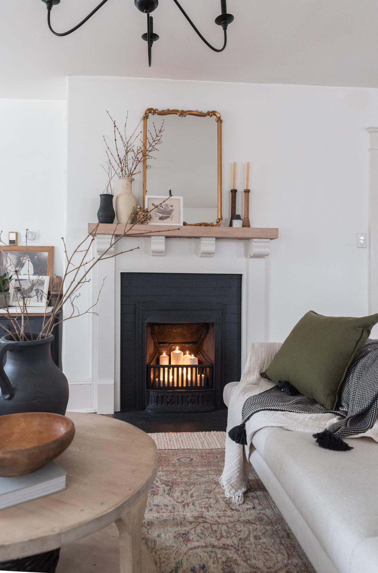 The Wild Decoelis | how to decorate for winter | cream couch with vintage wool rug layers over cream braided rug. wool pillows, sticks in a vase, fireplace with candles
