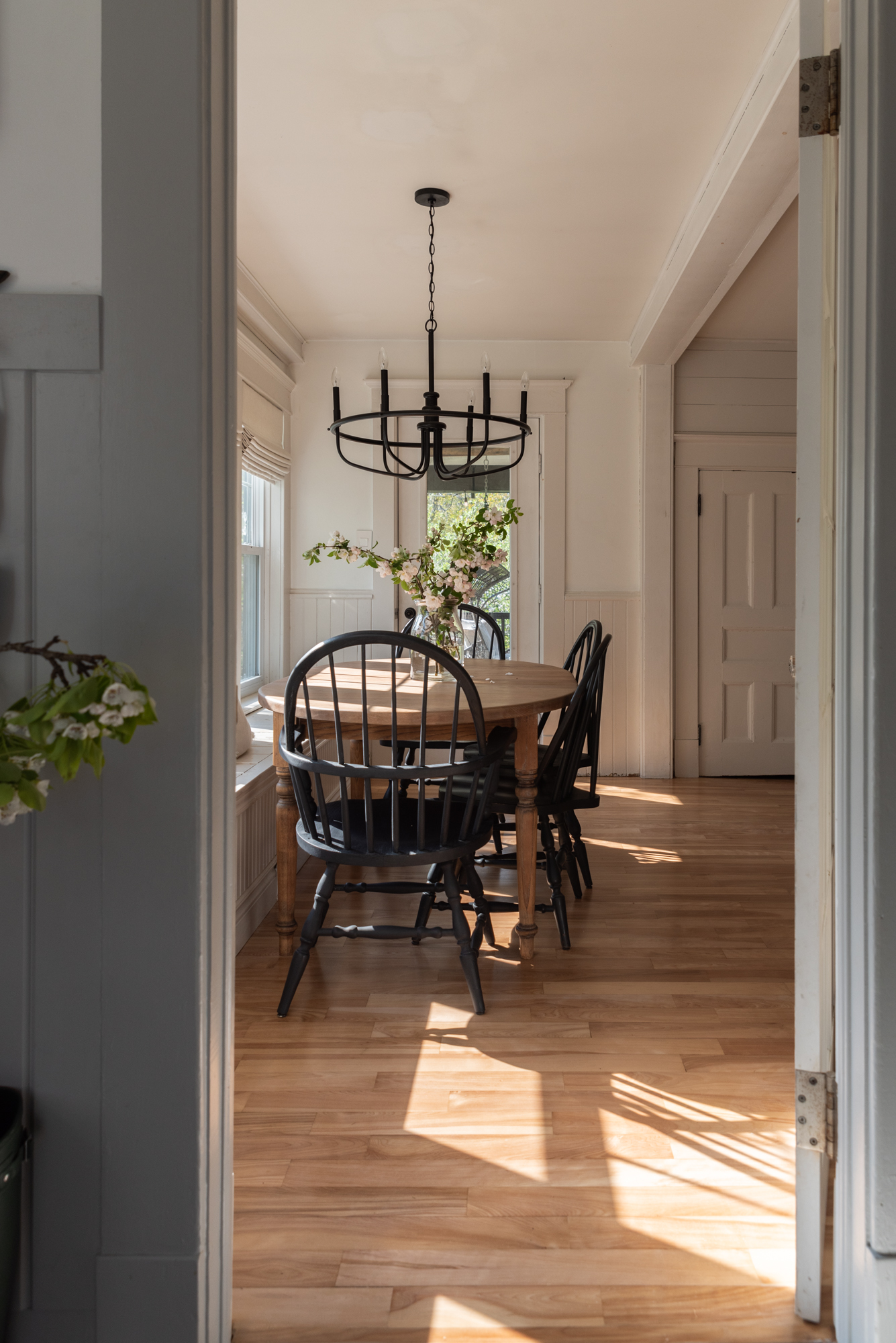 the wild decoelis | apple blossom branches in the house as decorations. Built in bench, refinished wood floors, black chairs, baskers, black vase, black chandelier, vintage art.