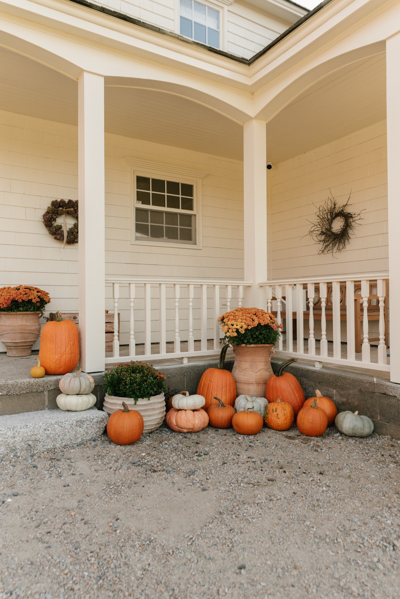 Fall pumpkins and potted mums arranged on a historic farmhouse porch with cream siding and Hinkley lighting.